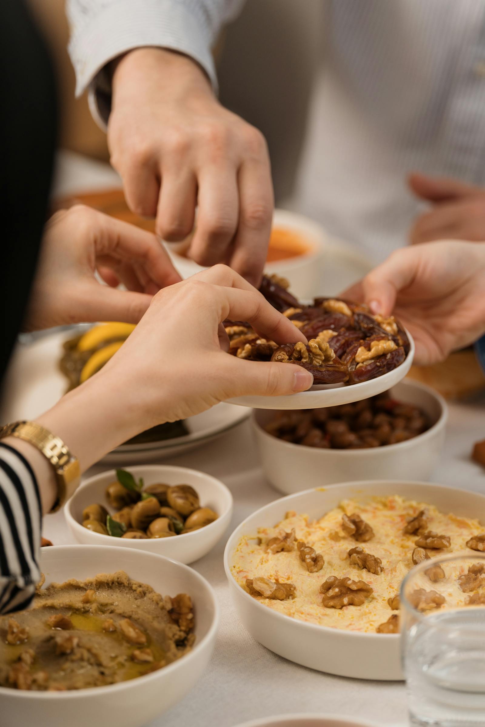 Hands reaching toward shared Mediterranean dishes during a communal restaurant meal.